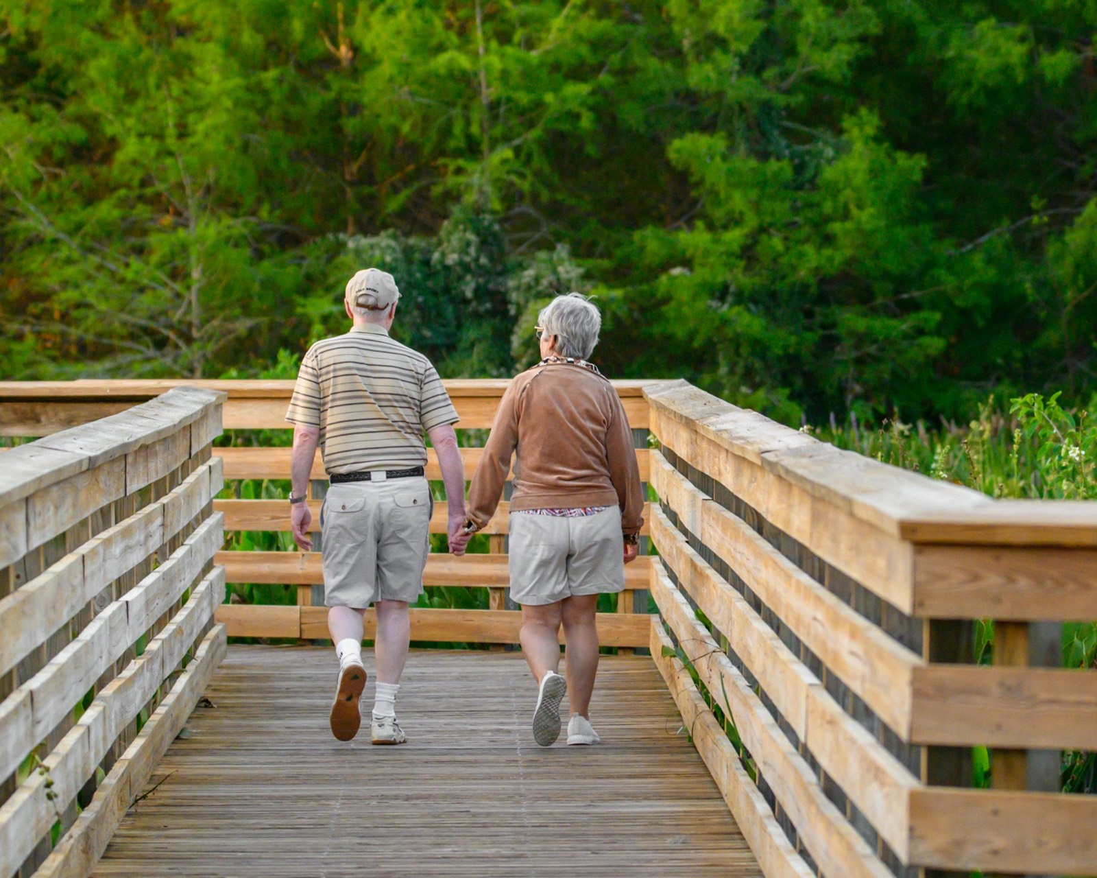 An older couple walking along a wooden boardwalk among trees